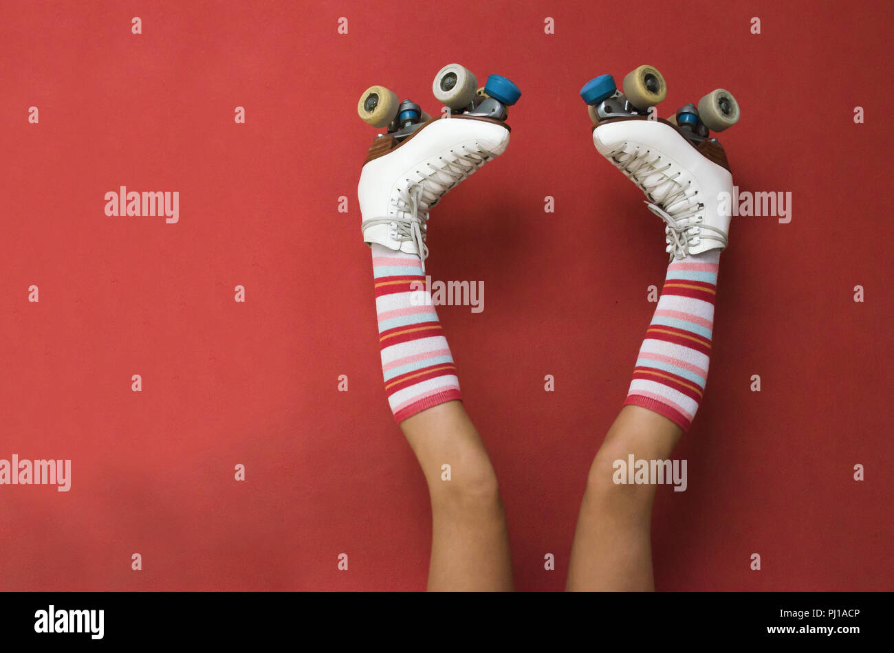 Girl's legs wearing long socks and rollerskates upside down against a wall Stock Photo