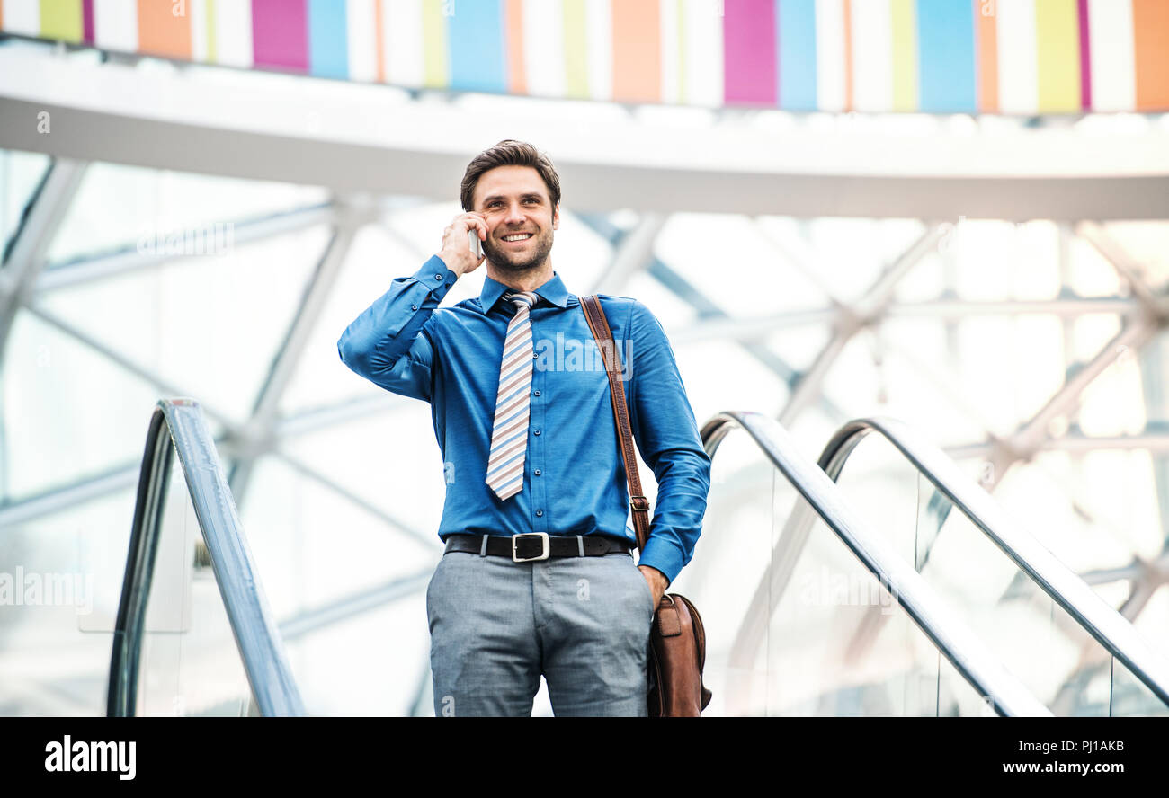 A young businessman going down escalator, talking on the phone. Copy space. Stock Photo