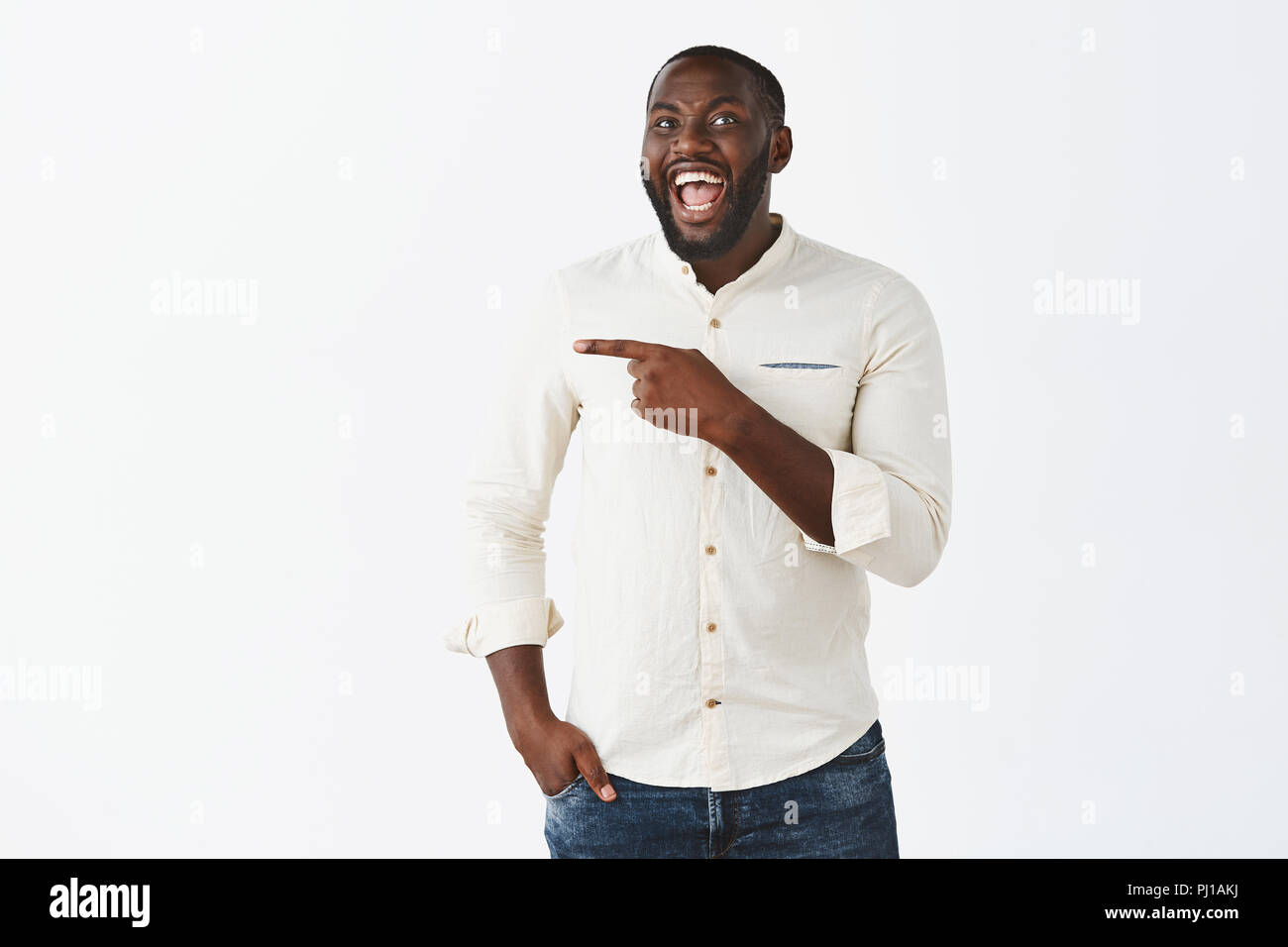 Ha-ha look at that weirdo. Portrait of happy emotive good-looking dark-skinned man with beard, laughing out loud joyfully, having fun on party, wearing trendy clothes and pointing left with forefinger Stock Photo