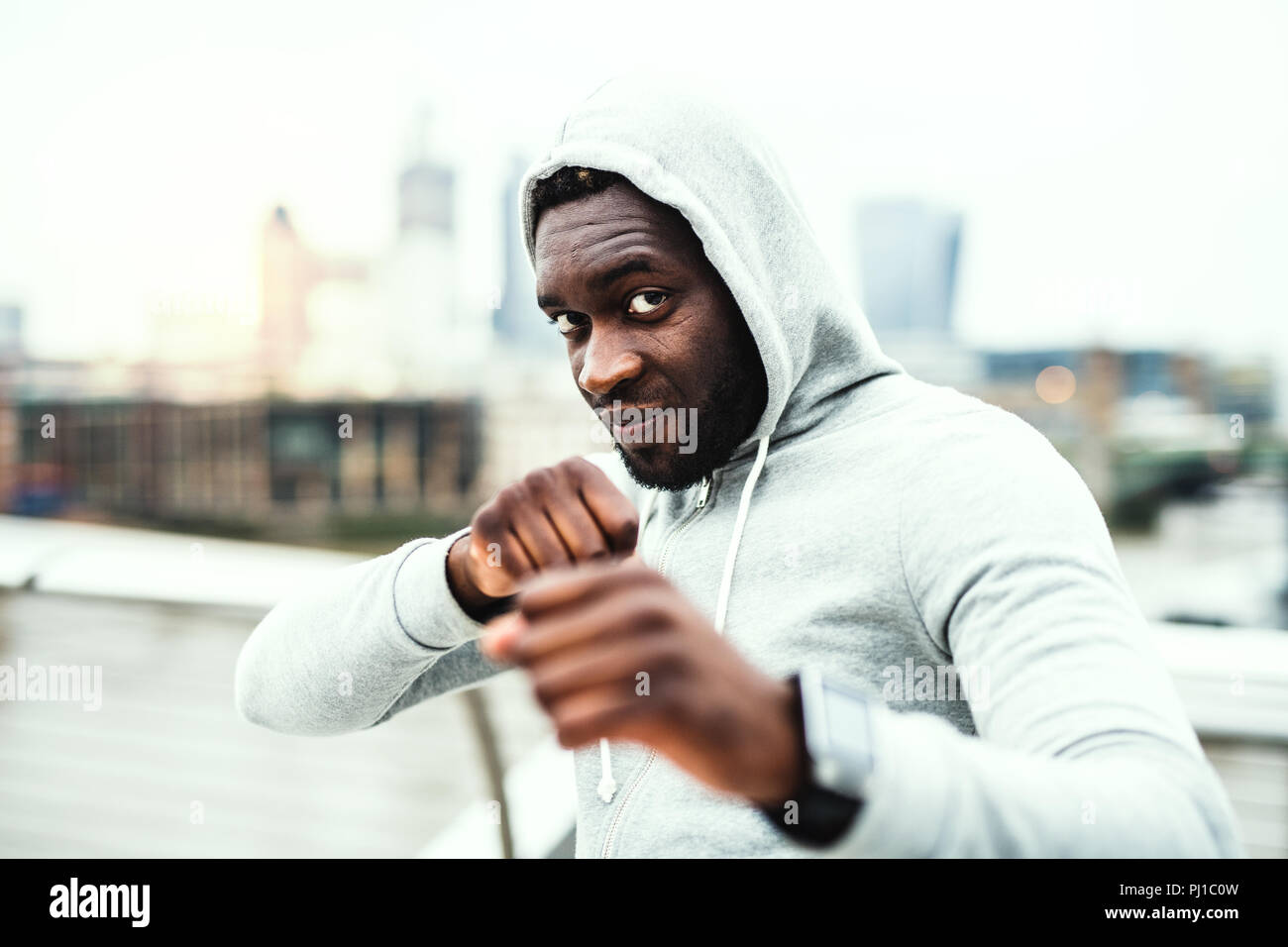 Young active black sportsman in boxing position in a city, wearing hoodie. Stock Photo