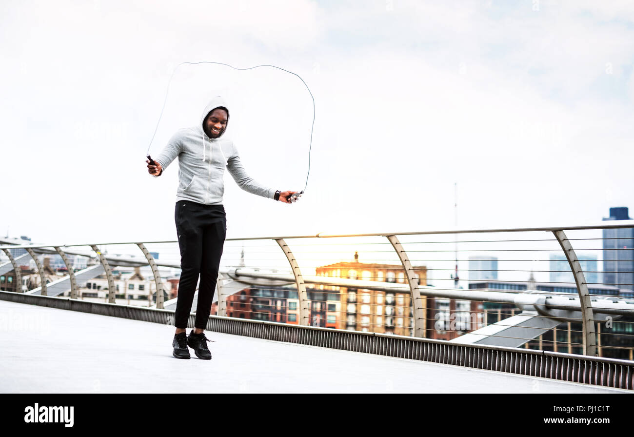 Young active black sportsman skipping with a rope in a city, wearing hoodie. Stock Photo