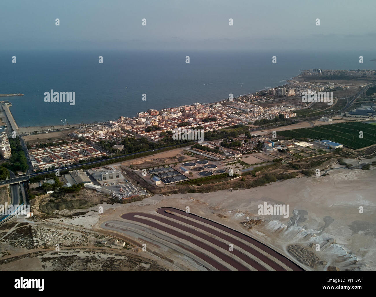 Panoramic aerial view of Torrevieja cityscape and Las Salinas, pink lake at sunset, evening light. Residential houses roofs, townscape and Mediterrane Stock Photo