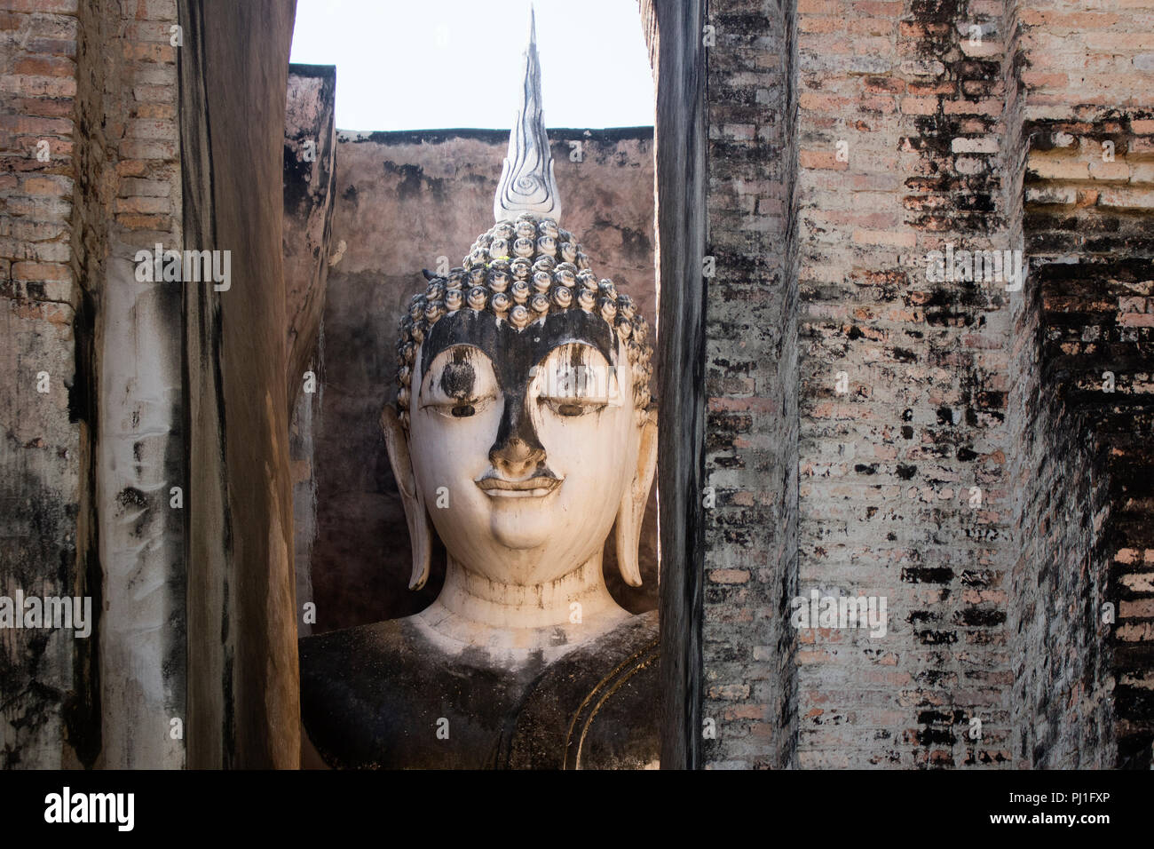 Ancient buddha head peeking from Wat Si Chum temple in Sukhothai Historical Park, Thailand Stock Photo