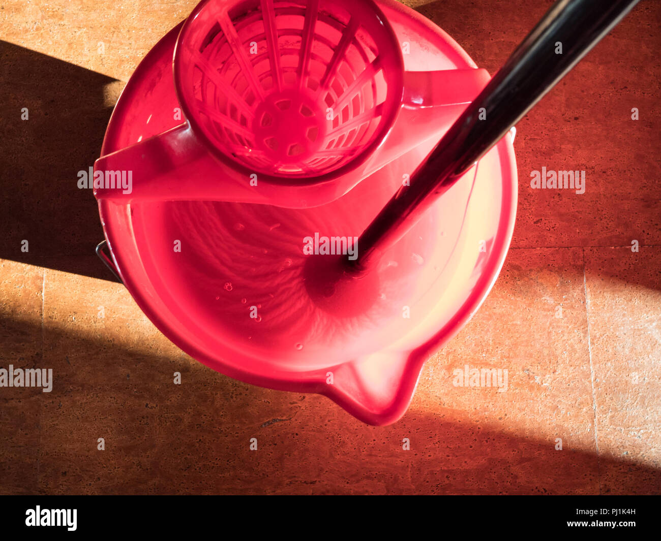 top view of wetting a mop in red bucket of water illuminated by