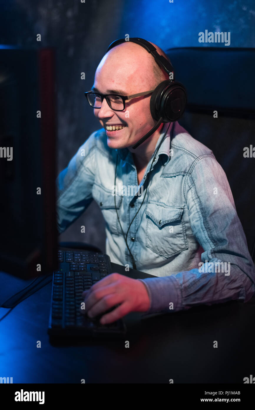 Excited handsome young gamer in glasses and earphones playing computer game and shouting at home Stock Photo