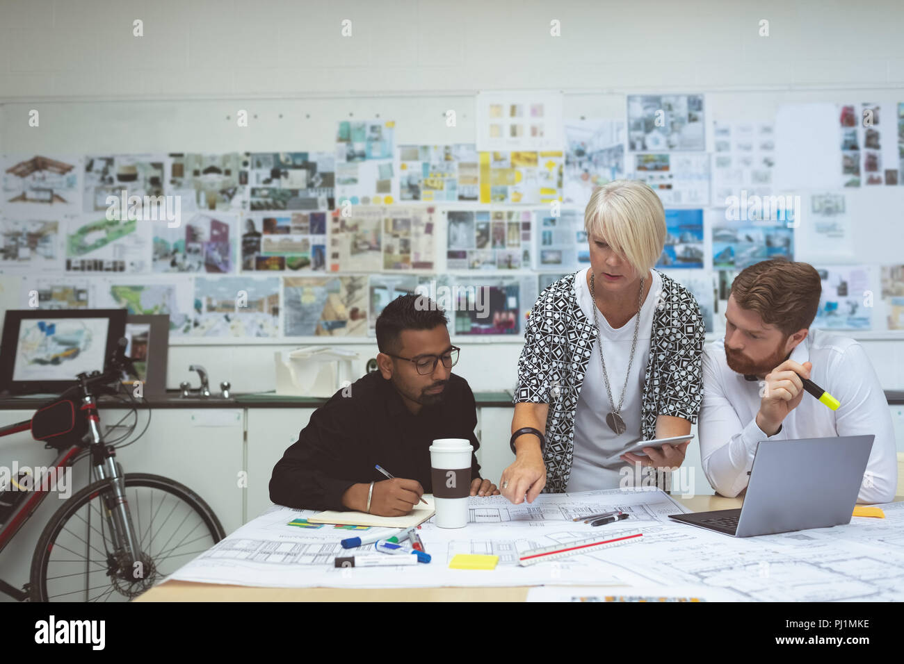 Executives discussing over blueprint at desk Stock Photo