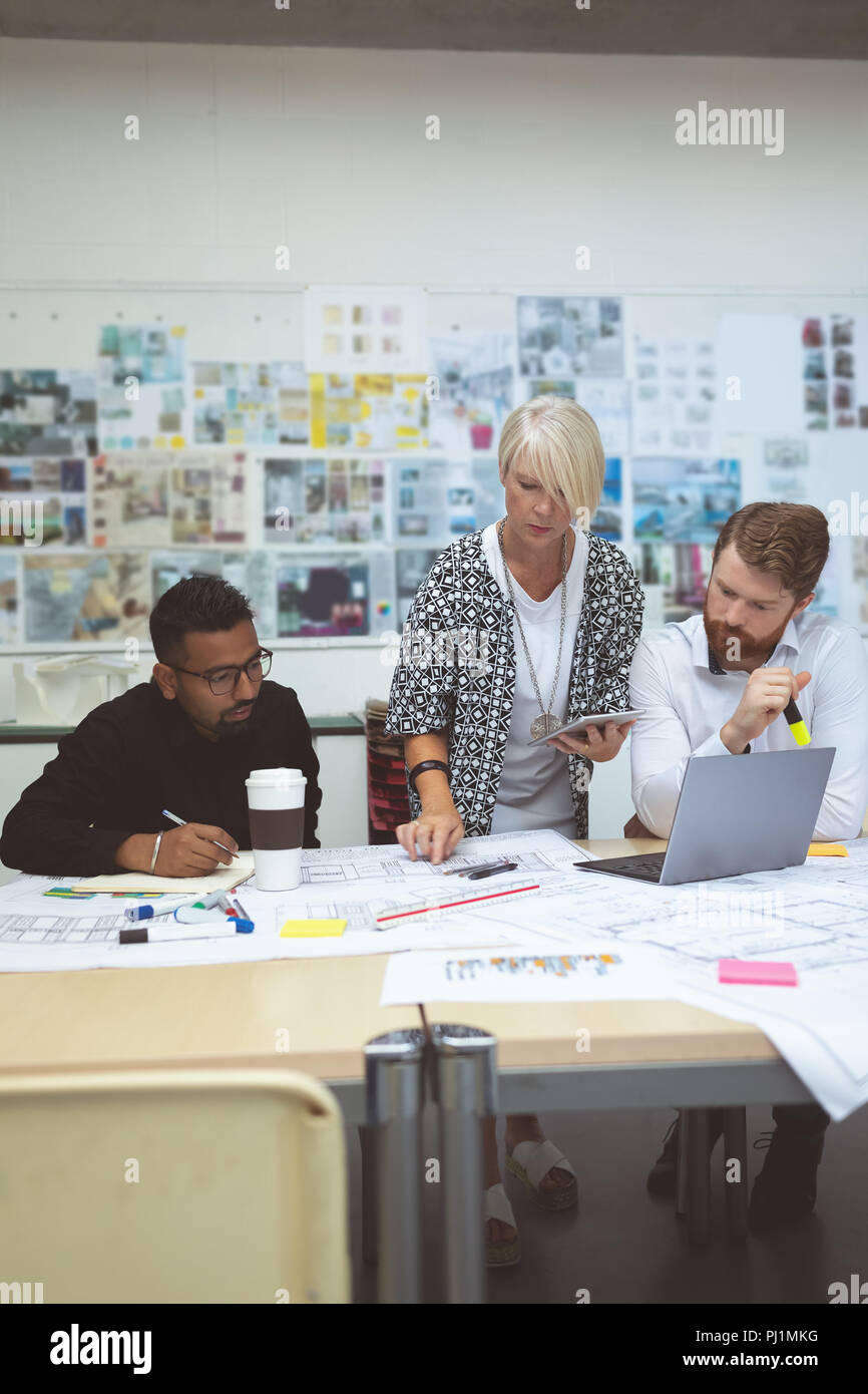 Executives discussing over blueprint at desk Stock Photo