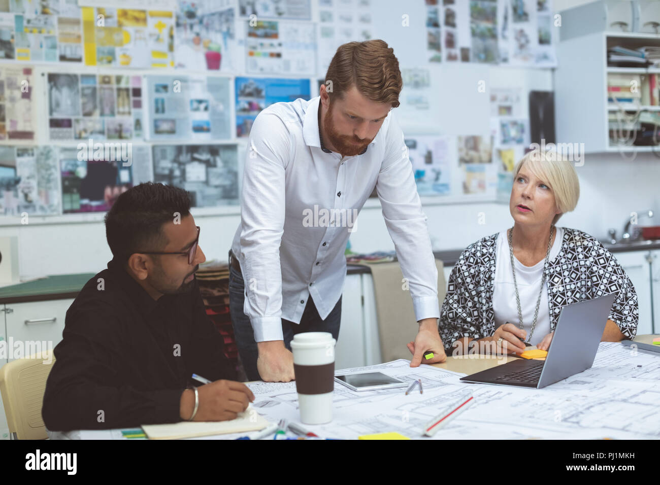 Executives discussing over blueprint at desk Stock Photo