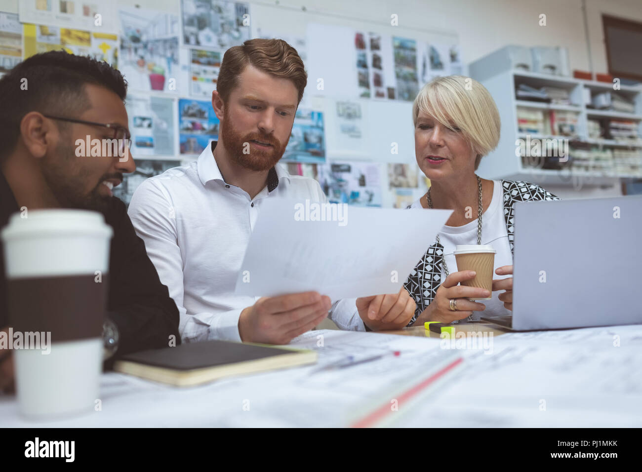 Executives discussing over blueprint at desk Stock Photo
