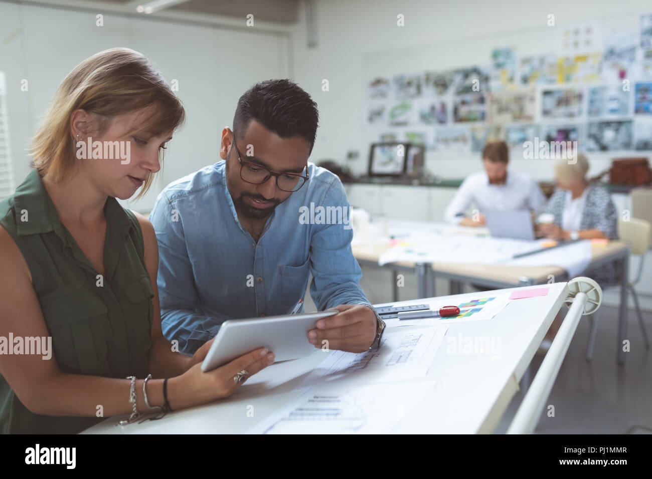 Executives discussing over digital tablet on drafting table Stock Photo