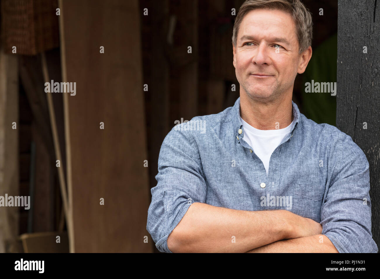 Portrait shot of an attractive, successful and happy middle aged man male wearing a blue shirt leaning on a post by a garage or barn Stock Photo
