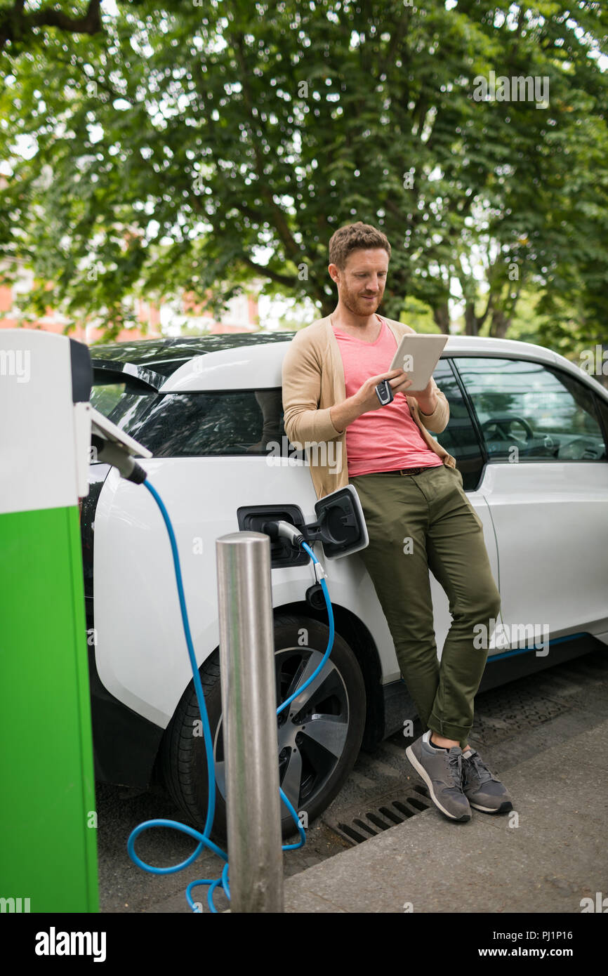 Man using digital tablet while charging electric car Stock Photo