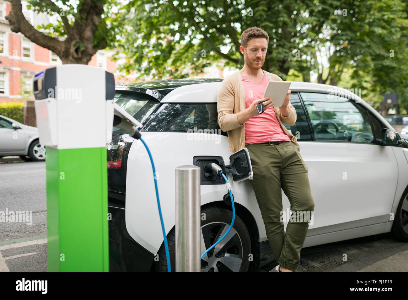 Man using digital tablet while charging electric car Stock Photo