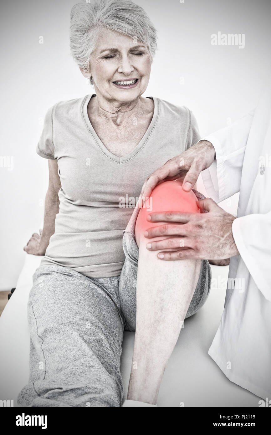 Composite image of displeased senior woman getting her knee examined Stock Photo