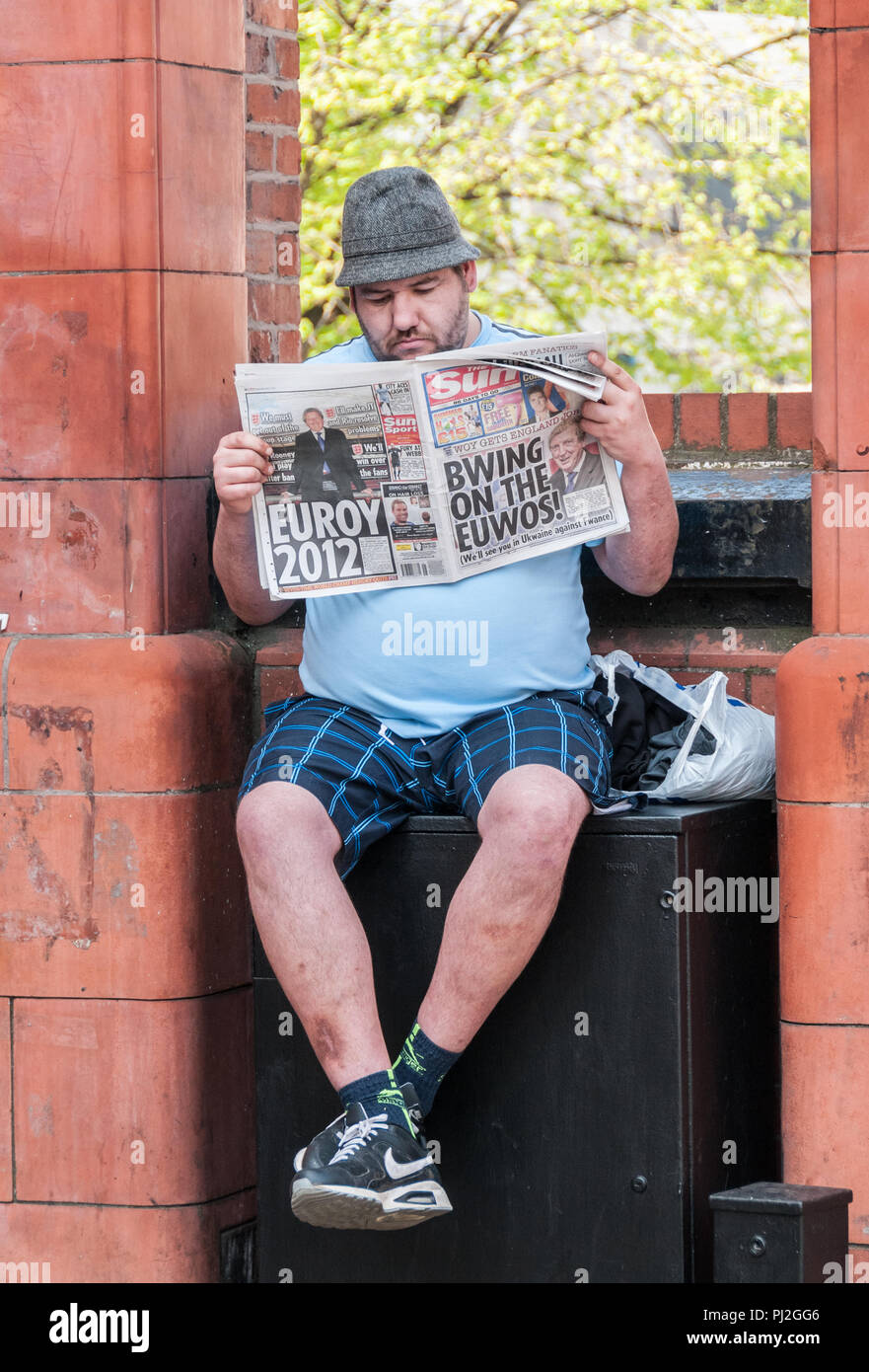 Man wearing trilby hat and shorts sat on wall in Manchester reading the Sun newspaper from 2012 before the Euro football tournament Stock Photo
