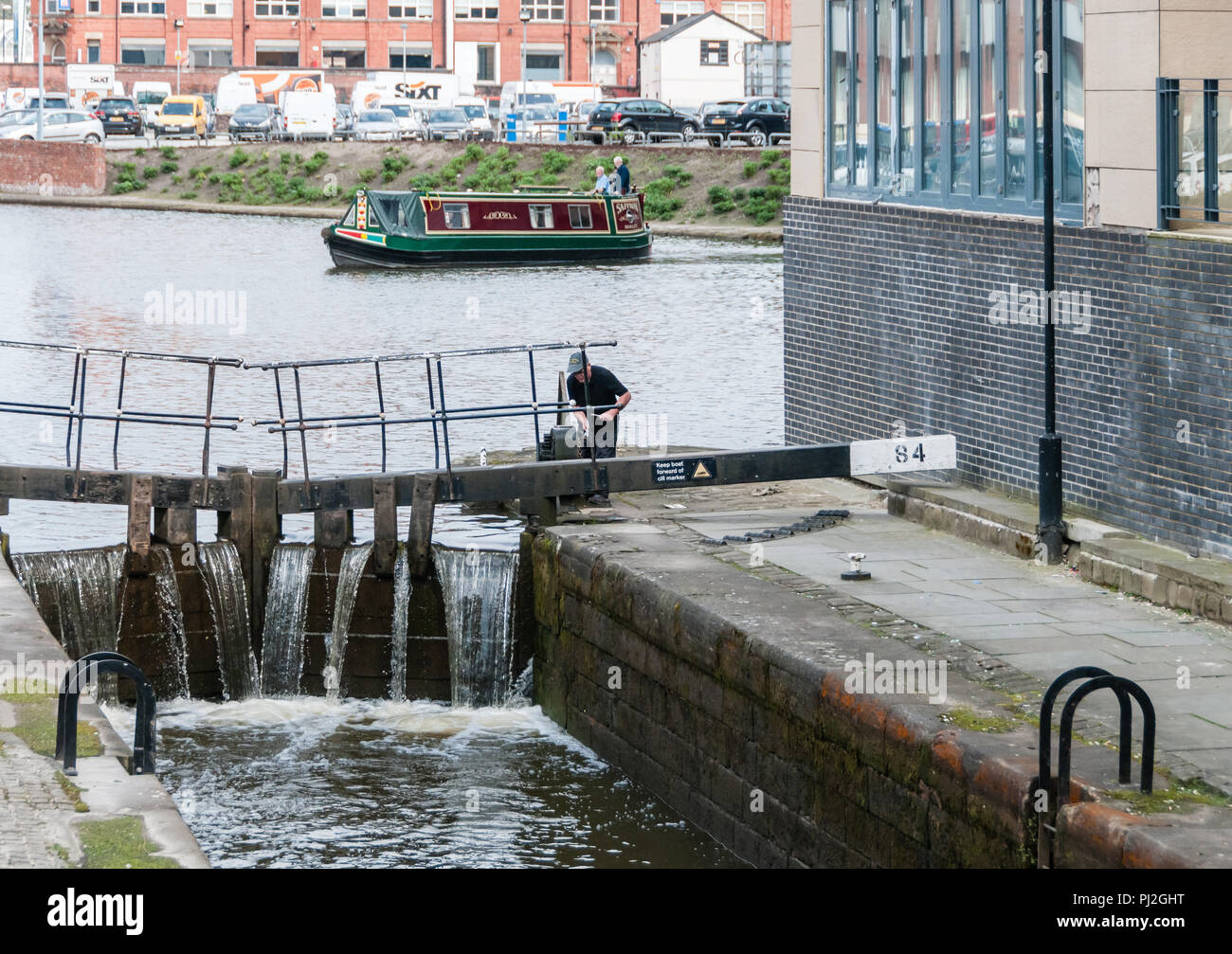 Man attending to a lock on a canal in Manchester with a narrowboat in the distance Stock Photo