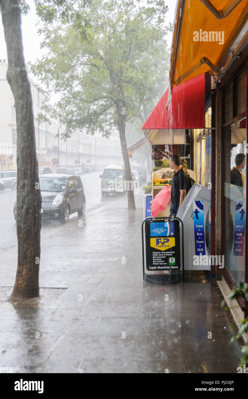 People stood under shop awning in Pimlico, London, to avoid a heavy rain shower Stock Photo