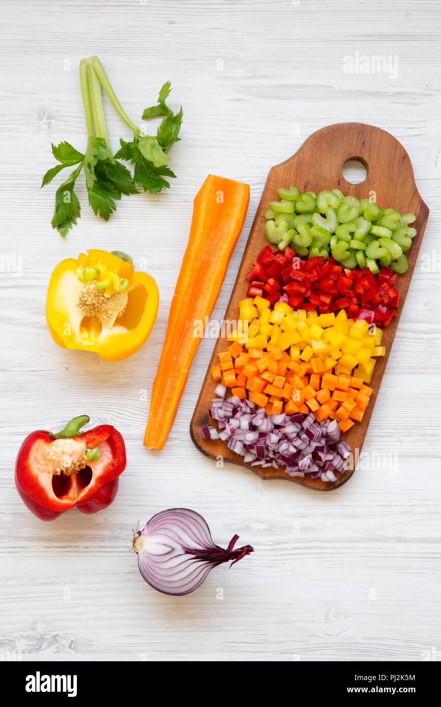Chopped vegetables (carrot, celery, red onion, peppers) arranged on cutting board on white wooden table, high angle view. Stock Photo