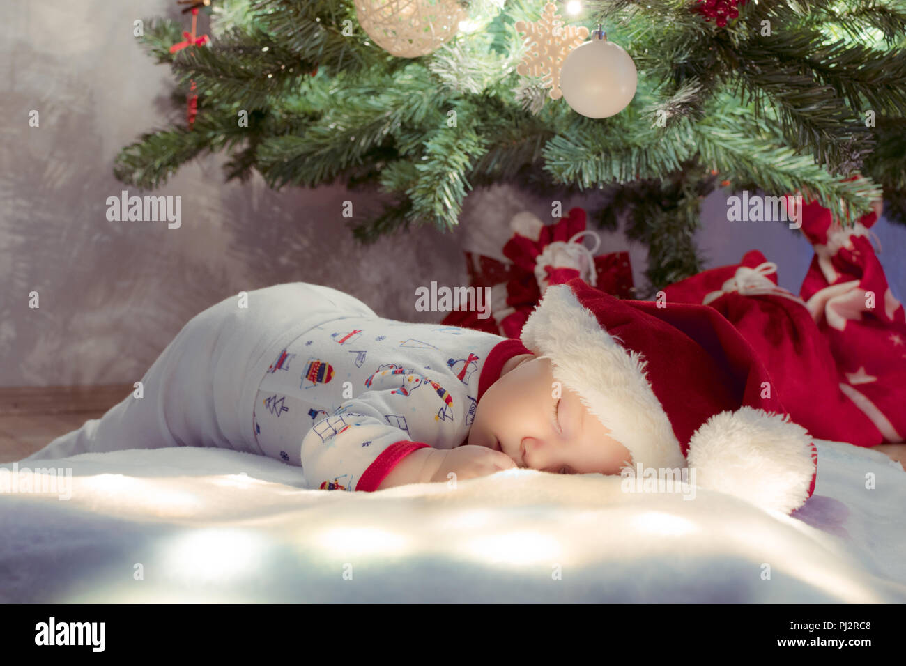 Sweet newborn baby boy sleeping and dreaming under Christmas tree. Stock Photo