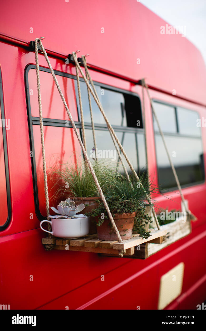 Homemade DIY shelving made out of wood and wooden crates and hung from rope supports on the side of a camper van (van). Alternative lifestyle garden. Stock Photo