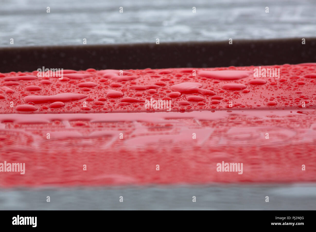Raindrops pooled together on top of a red barrier Stock Photo