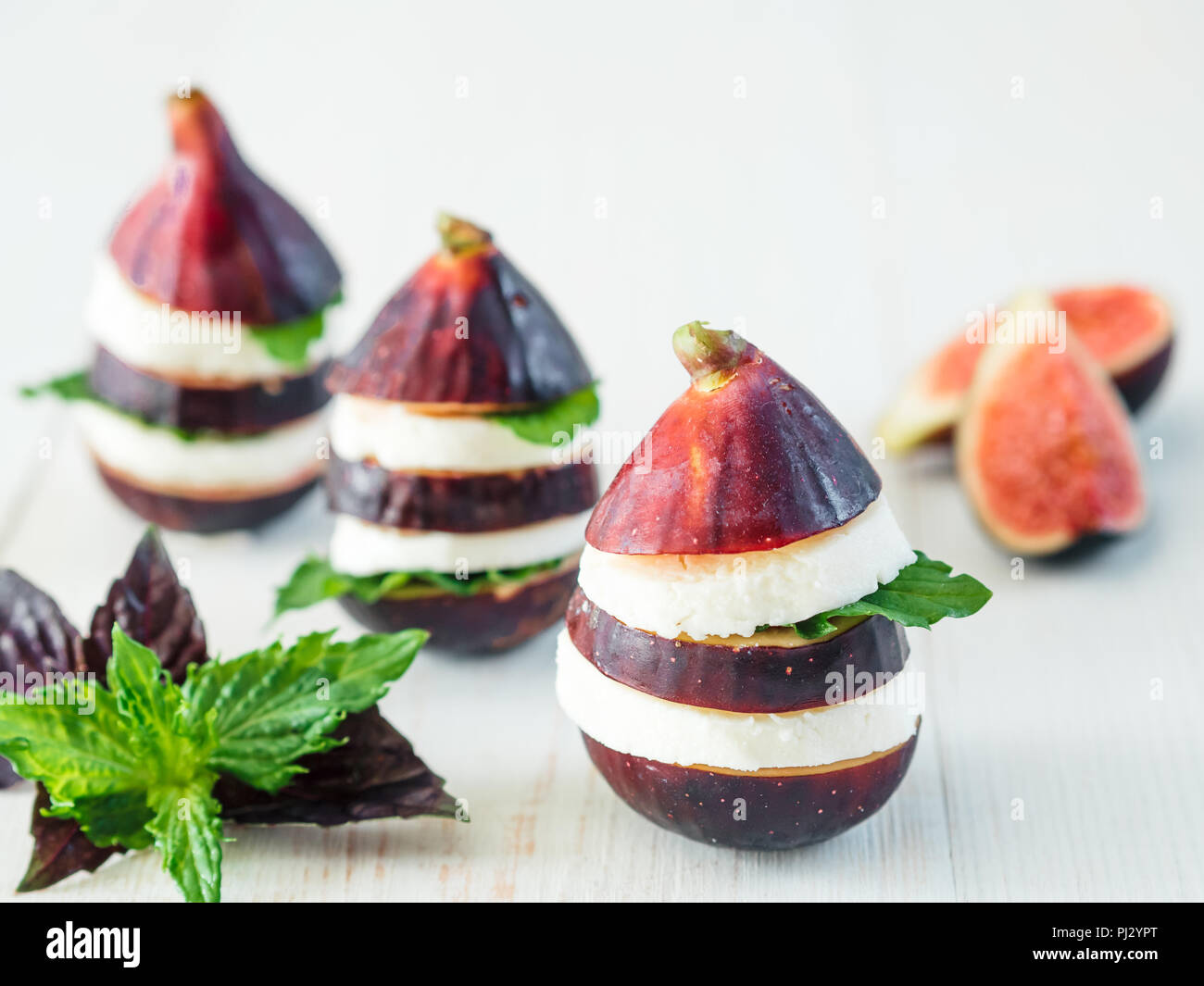 Ready-to-eat fun appetiezer with figs, cheese, purple basil and mint leaves. Ideas and recipes for healthy breakfast, dinner, appetiezer, salad. Can use for design cheese dairy. Copy space for text Stock Photo