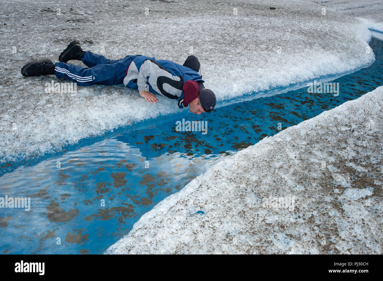Glacier helicopter tour and hike - Juneau Alaska a tourist in Alaska drinks glacial meltwater from the ice of Gilkey Glacier on the Juneau icefield Stock Photo