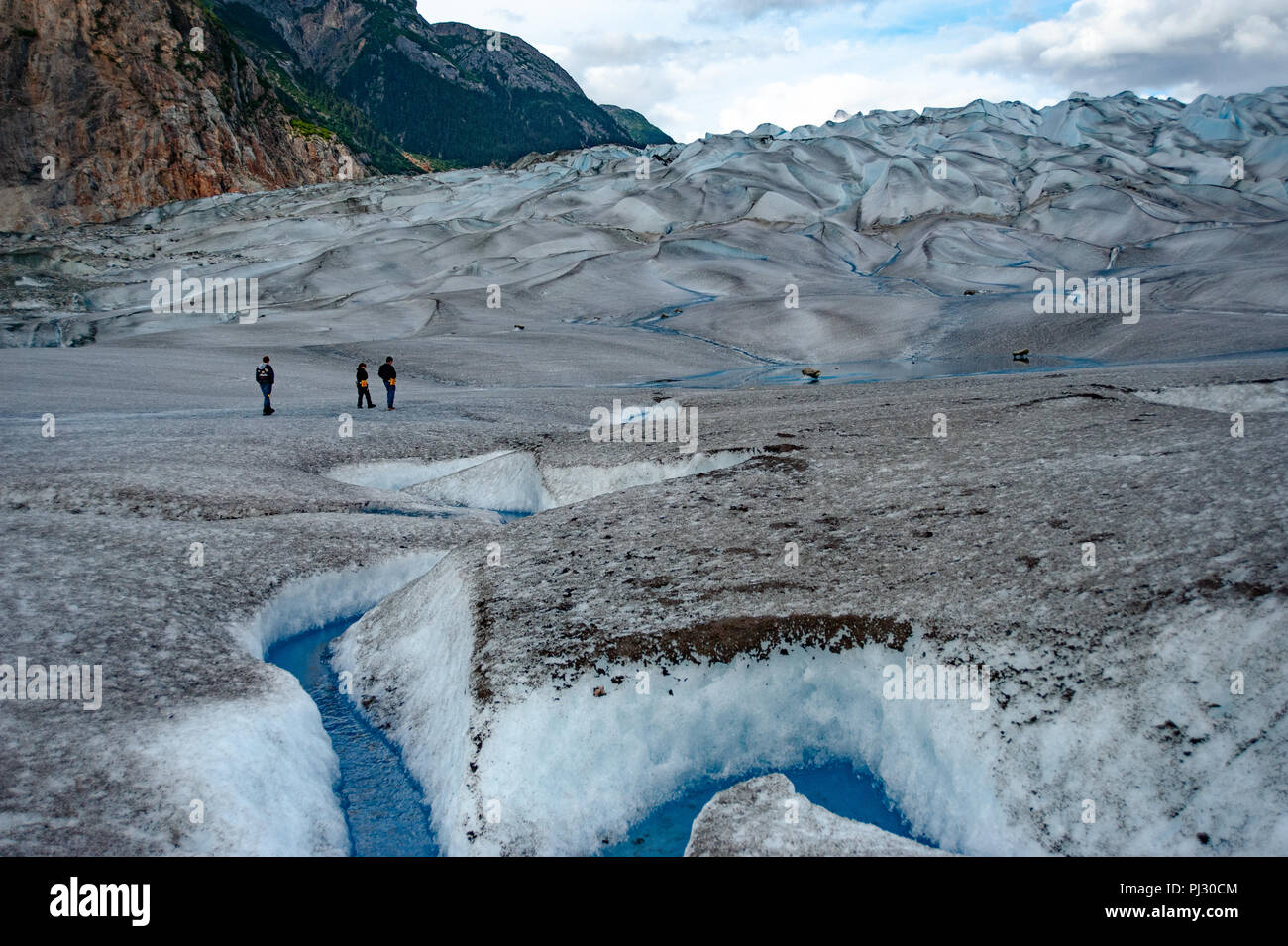 Glacier helicopter tour - Juneau Alaska - tourist hikers on a glacier hiking Gilkey Glacier on the Juneau icefield - blue glacial meltwater Stock Photo