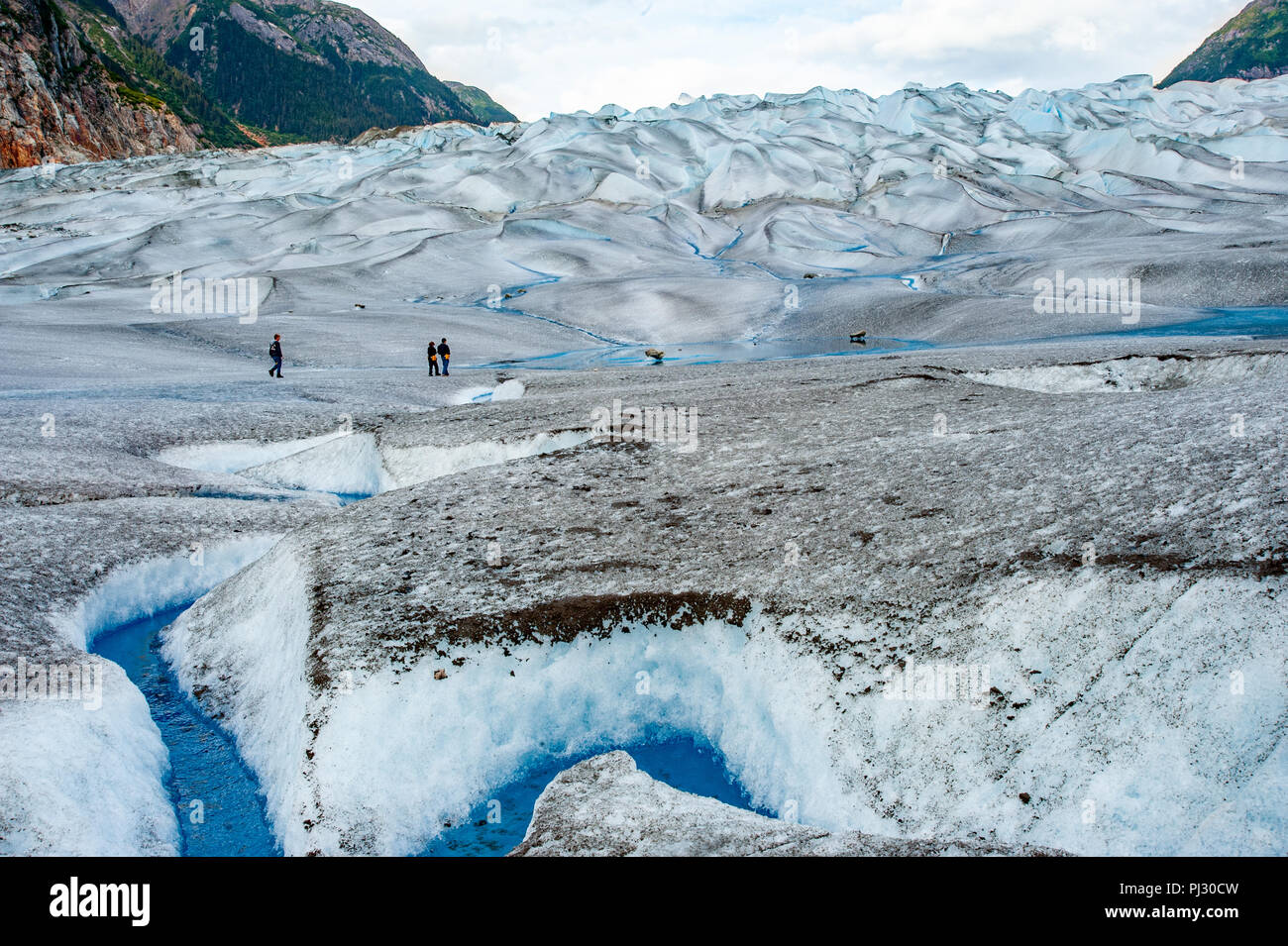 Glacier helicopter tour - Juneau Alaska - tourist hikers on a glacier hiking Gilkey Glacier on the Juneau icefield - blue glacial meltwater Stock Photo