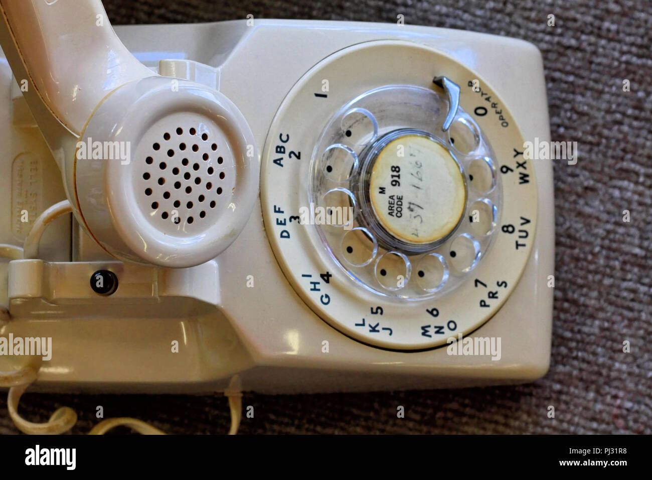 An old cream or beige Bell System analog rotary dial desk telephone sits with the receiver off the hook. Stock Photo
