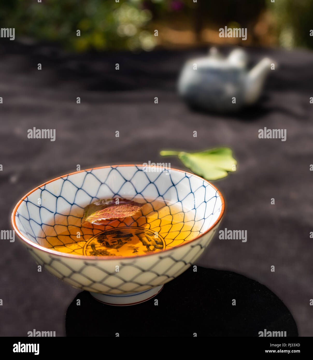 Japanese bowl filled with brown tea, in the background a deliberately blurred teapot. Stock Photo