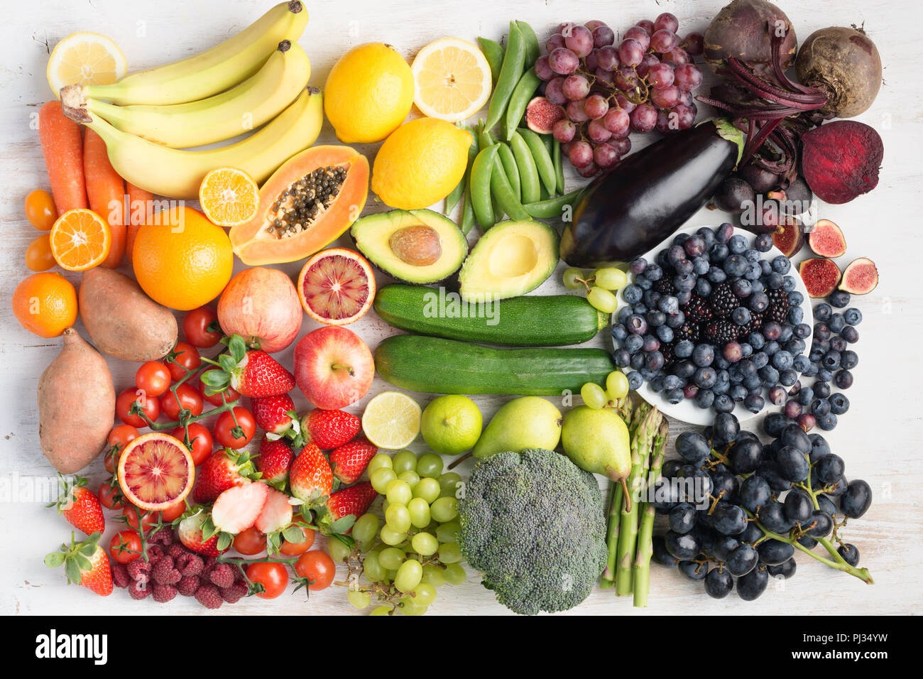 Healthy eating concept, assortment of rainbow fruits and vegetables, berries, bananas, oranges, grapes, broccoli, beetroot on the off white table arranged in a rectangle, top view, selective focus Stock Photo
