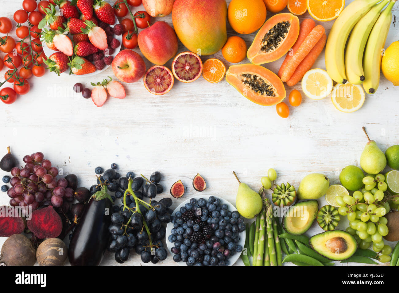 Healthy eating background, different varieties of colourful fruits and vegetables in rainbow colours on the off white table with copy space in the middle, top view, selective focus Stock Photo