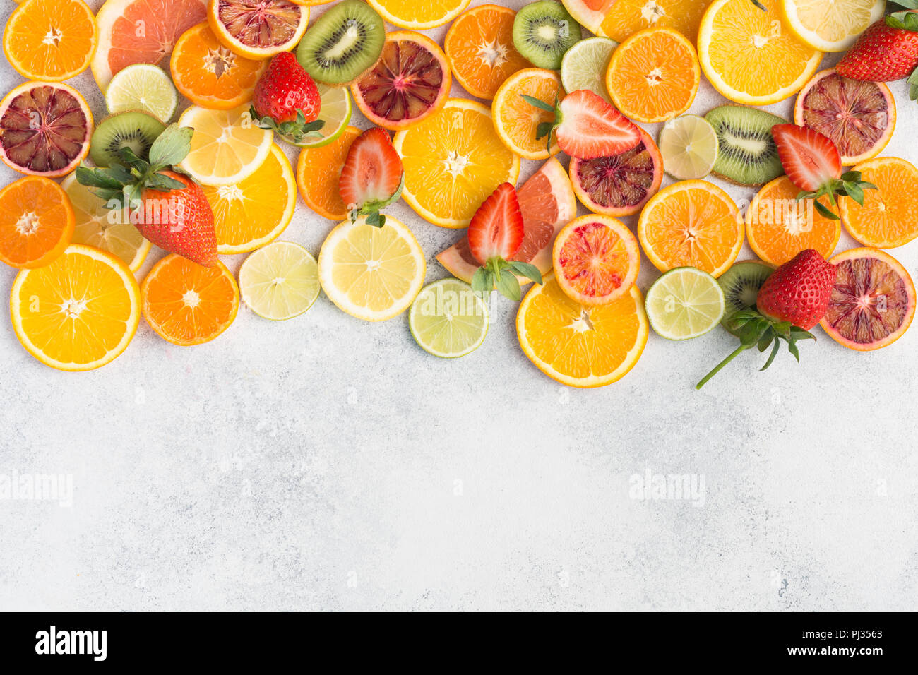 Colourful fruits background, oranges, clementines, blood oranges, kiwis, strawberries and grapefruits on white table background, top view, copy space for text, selective focus Stock Photo