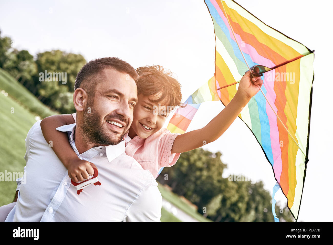 Weekend activities. Father carrying son on his back holding kite Stock Photo