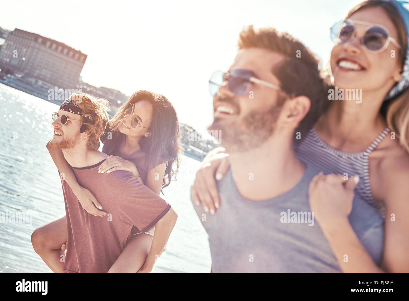 Outdoors photo of happy boyfriends piggybacking their girlfriends at sunset on beach Stock Photo