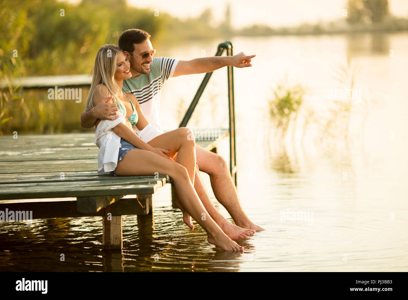 Romantic couple sitting on the wooden pier on the lake at sunny day ...