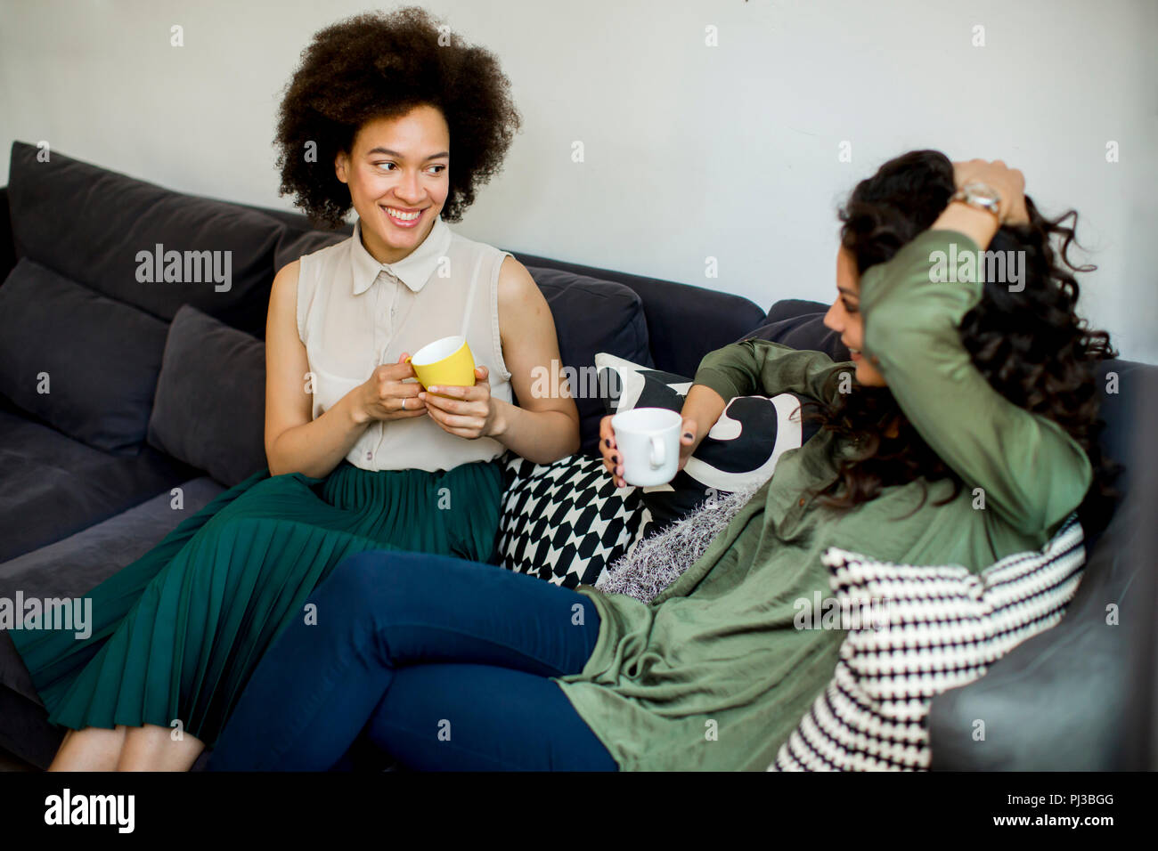 Two multiracial young women chatting and drinking coffe in rhe living room Stock Photo