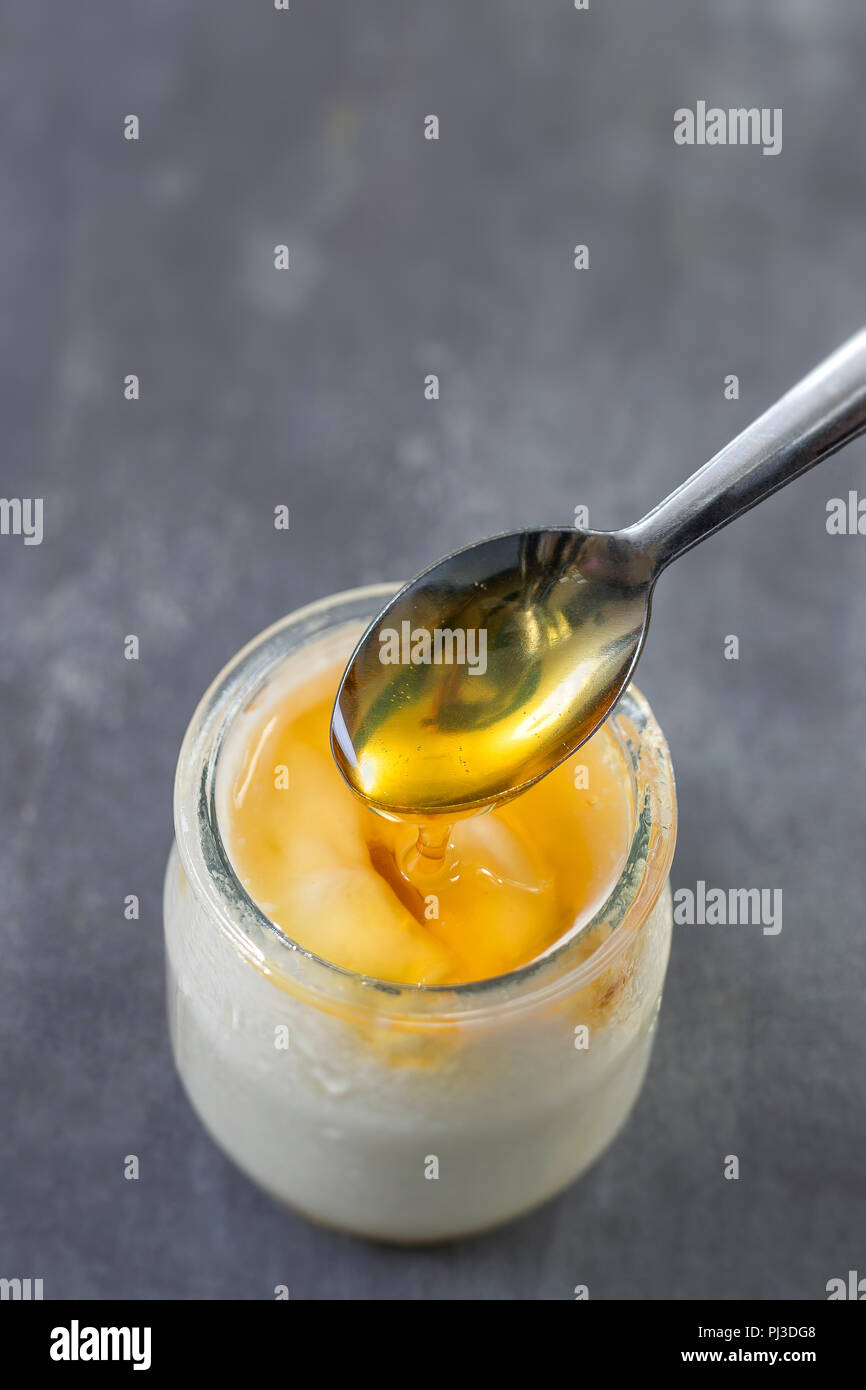 Honey Yogurt. Yogurt and pouring honey in glass jar on slatte background Stock Photo