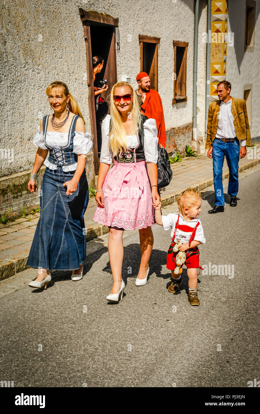A woman traditionally dressed in a dirndl navigates the streets of Reith bei Seefeld, Austria holding the hand of her young son in lederhosen Stock Photo