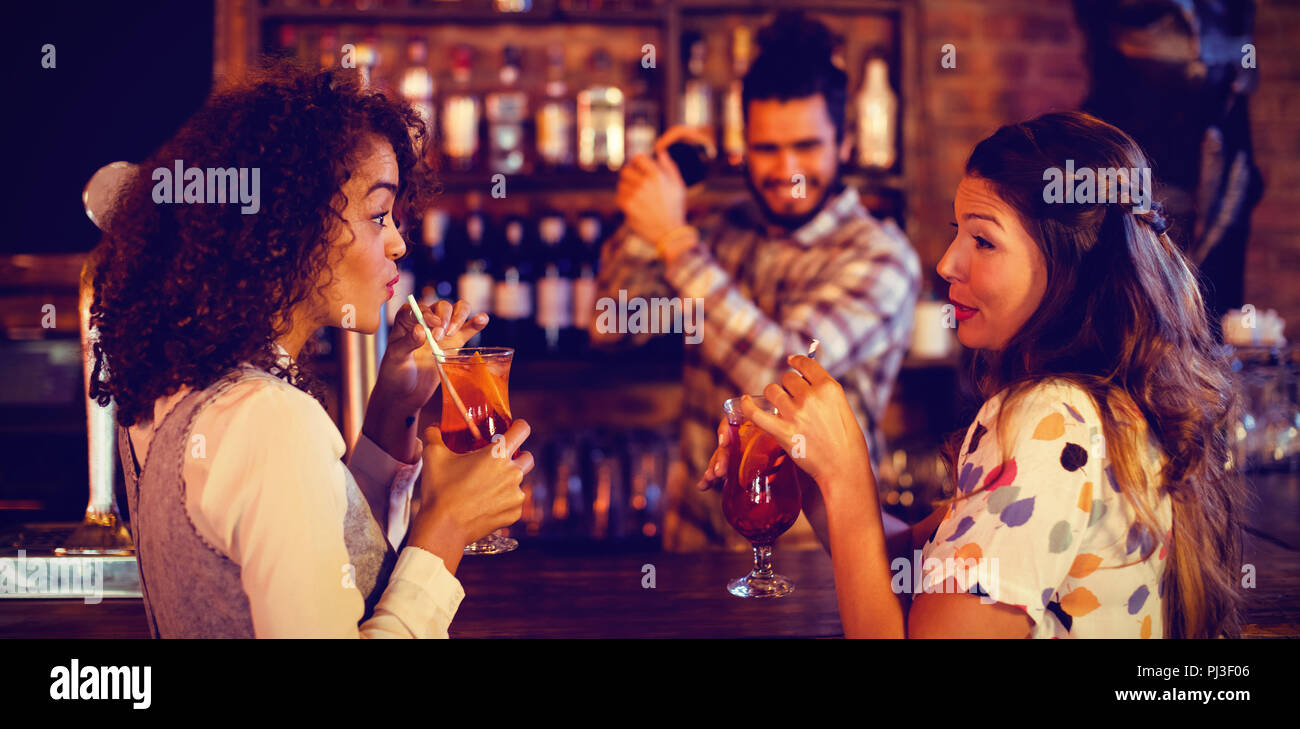 Two young women having cocktail drinks at counter Stock Photo