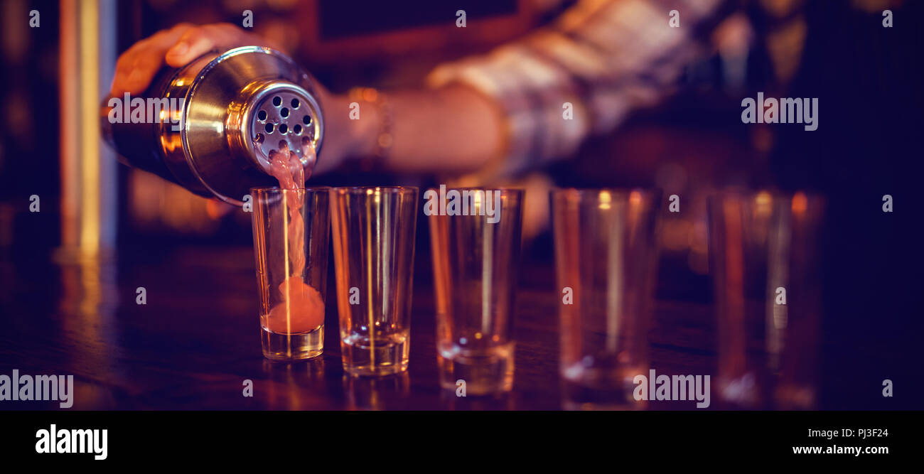 Waiter pouring cocktail drink into shot glasses at counter Stock Photo