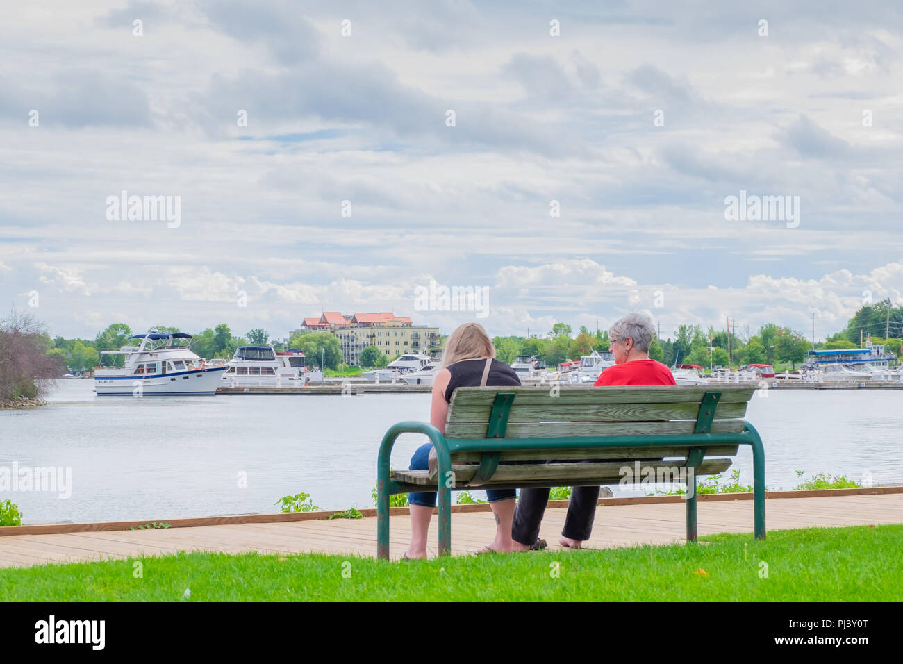 Two women sit on a bench near the boardwalk along the shore of Lake Couchiching at Orillia Ontario Canada. Stock Photo