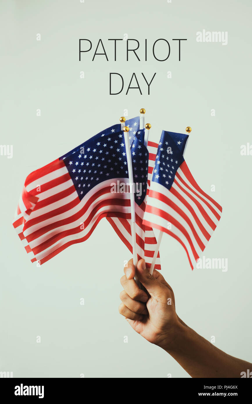 closeup of a young caucasian man with some american flags in his hand and the text patriot day, against an off-white background Stock Photo