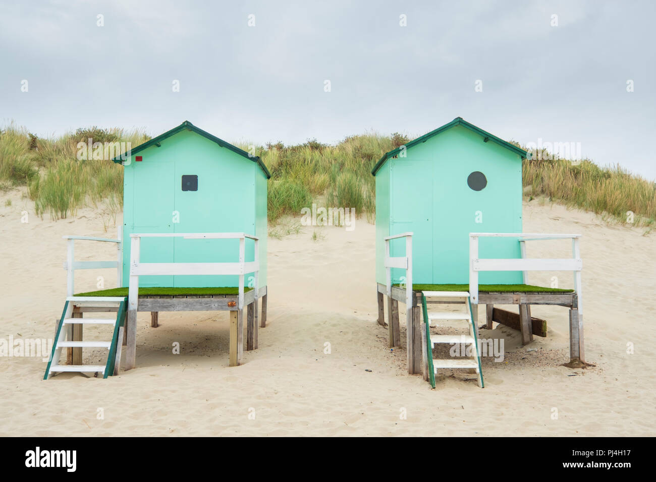 small beach houses with steps and a gate with in the background dunes with dune grass under a cloudy sky Stock Photo