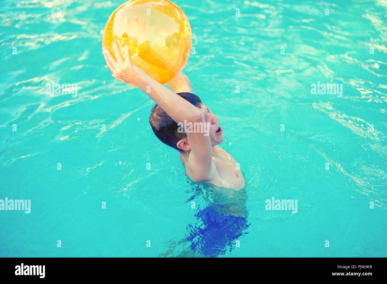 Little boy holding beach ball over head in swimming pool outdoor, summer activity Stock Photo