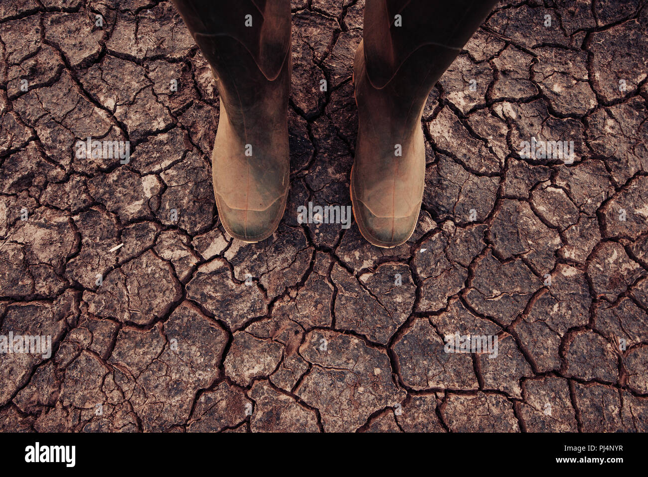 Farmer in rubber boots standing on dry soil ground, global warming and climate change is impacting crops growing and yield Stock Photo