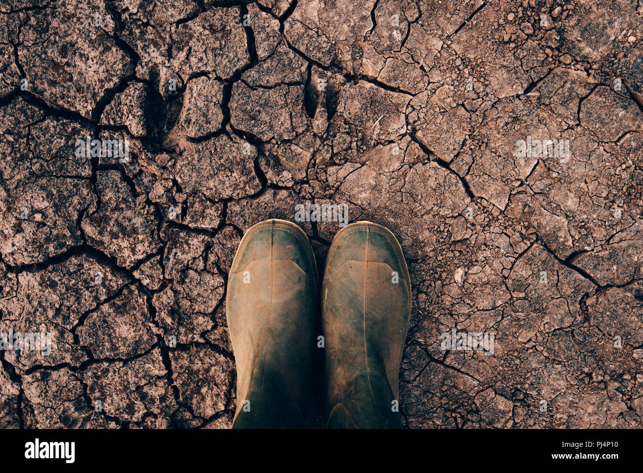 Farmer in rubber boots standing on dry soil ground, global warming and ...