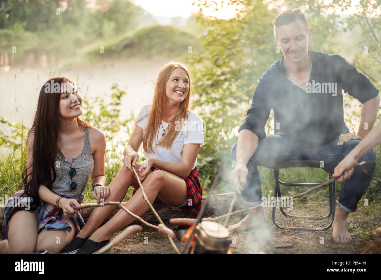 cheerful girls and pleasant boy are cooking on bonfire Stock Photo