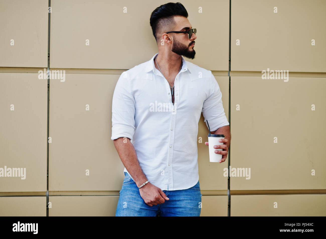 Stylish tall arabian man model in white shirt, jeans and sunglasses posed  at street of city. Beard attractive arab guy with cup of coffee against gold  Stock Photo - Alamy